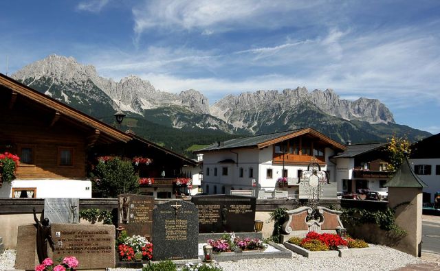 Ellmau in Tirol - der Kirchhof der Pfarrkirche zum Hl. Michael vor alpenländischen Häusern mit dem Wilden Kaiser im Hintergrund